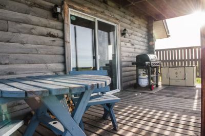 Wooden cabin deck with a blue table and bench and a BBQ grill.