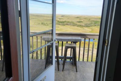 Open door leading to a balcony with a high table and two stools overlooking the coulees with a small spring.
