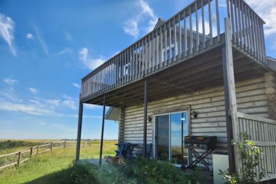 Exterior view of a wooden cabin with an elevated deck under a blue sky.