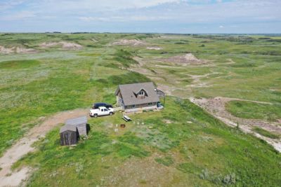 A cabin in an open grassy landscape under a partly cloudy sky.