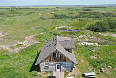 A rustic log cabin surrounded by green fields and natural landscape under a clear sky.