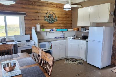 Cozy cabin kitchen with wooden walls, white cabinets, a refrigerator, stove, and a dining table with wooden chairs.