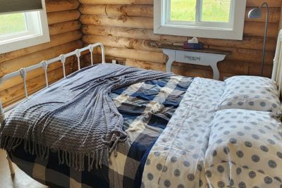 Cozy bed with patterned blankets and pillows inside a wooden log cabin room with a window.