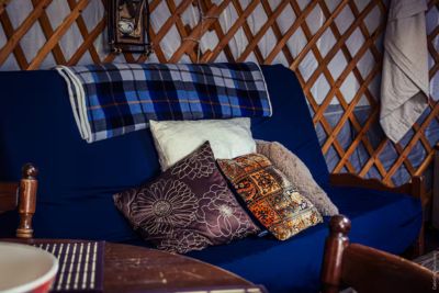 Cozy blue sofa inside a yurt with patterned cushions and a blue plaid blanket draped over the backrest.