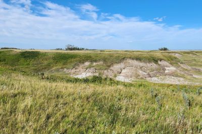 Grass-covered coulees under a partly cloudy blue sky.