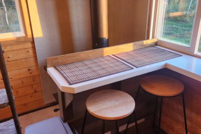 Cozy wooden corner breakfast nook with two round stools and two placemats on a white countertop by windows.