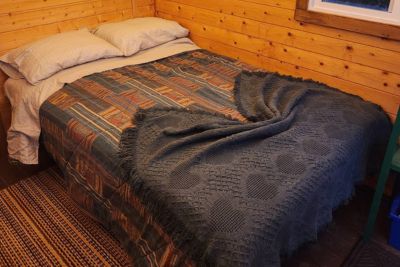 Cozy bed with patterned bedspread and dark textured blanket in a wood-panelled loft.