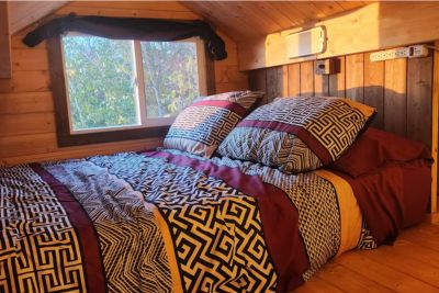 Cozy bed with patterned black, white, and burgundy bedding in a wooden cabin loft with a window.