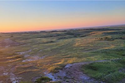 Wide grassy coulees under a clear sky at sunset.