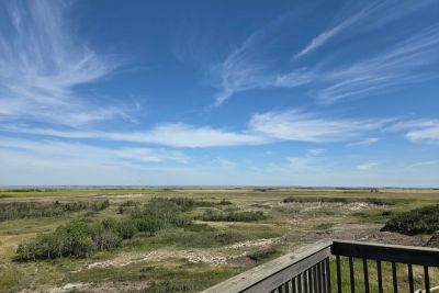 Wide open coulees under a blue sky with wispy clouds, viewed from a wooden balcony railing.