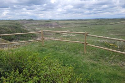 Wooden fence overlooking vast green coulees under a cloudy sky.