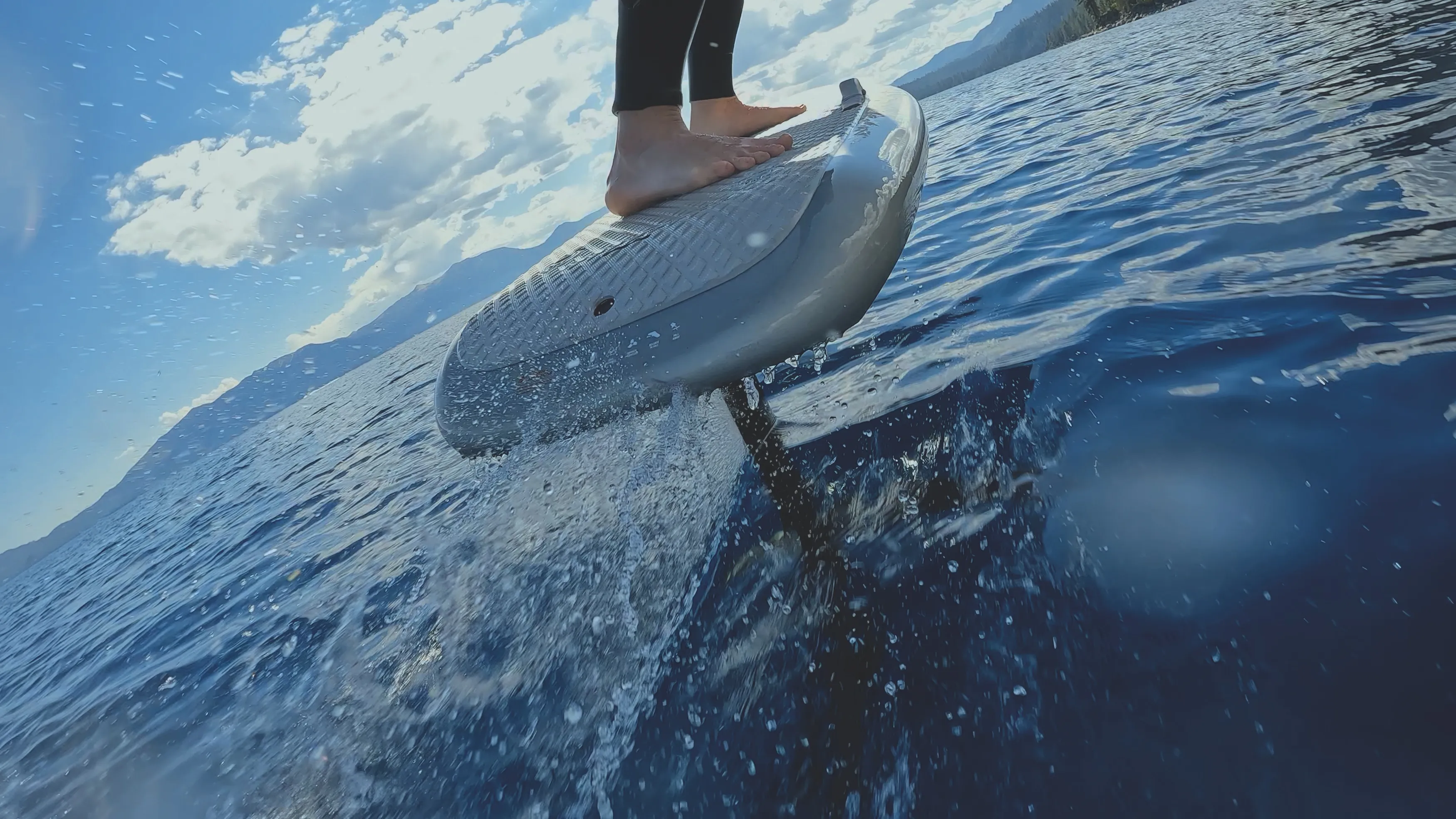 Close-up of a barefoot rider on an eFoil board lifting above deep blue Lake Tahoe water.