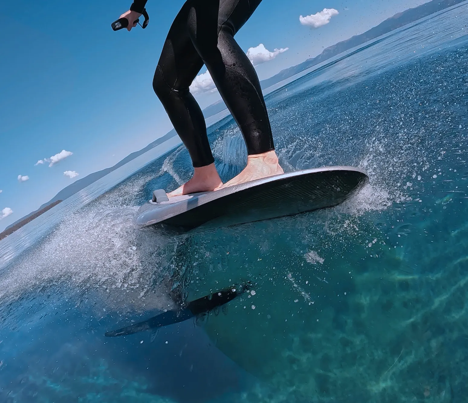 Low-angle view of an eFoil rider skimming over crystal-clear Lake Tahoe water, the hydrofoil visible below.