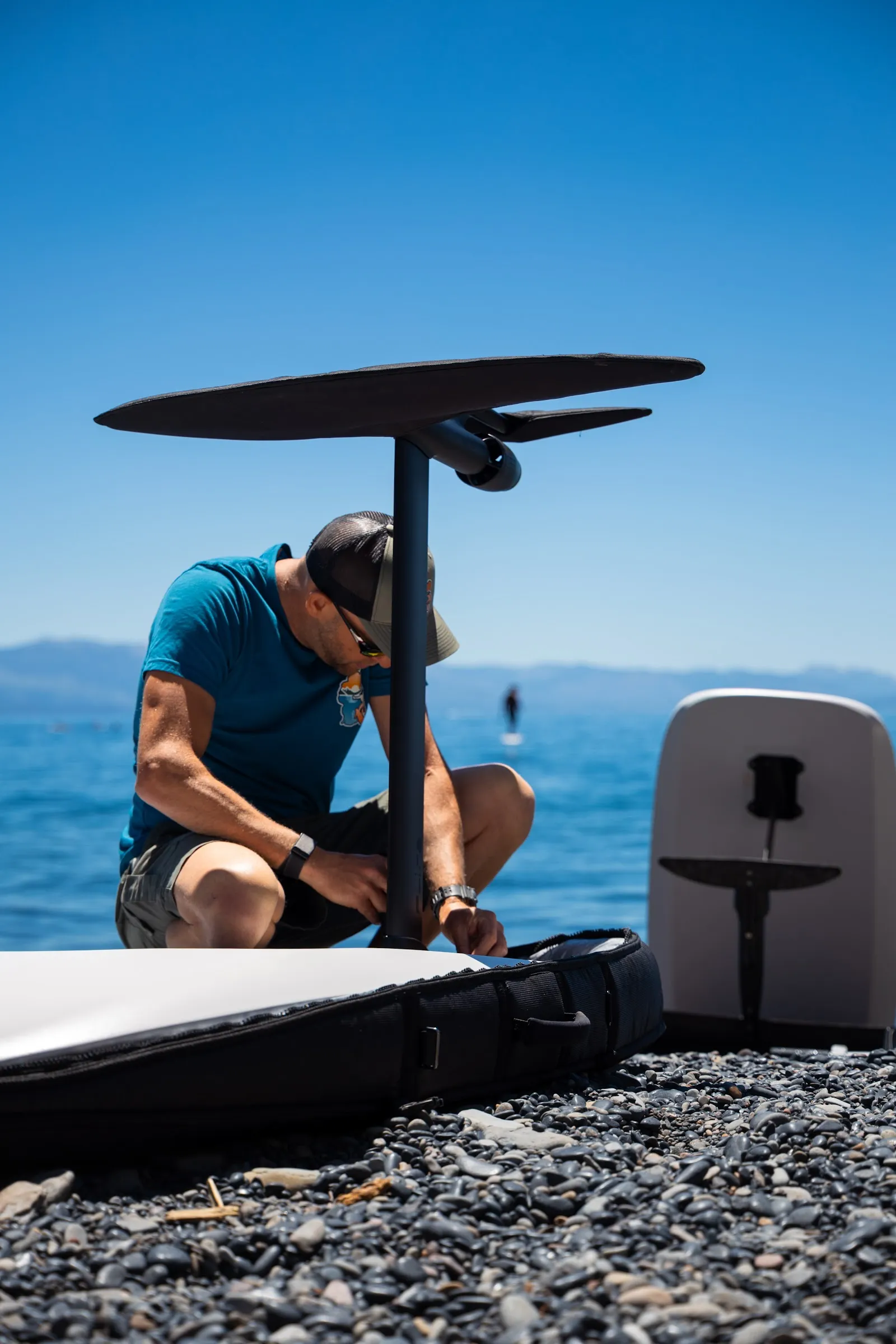 Efoil Tahoe technician assembling a Fliteboard mast and front wing on a rocky Lake Tahoe beach beside an open board bag