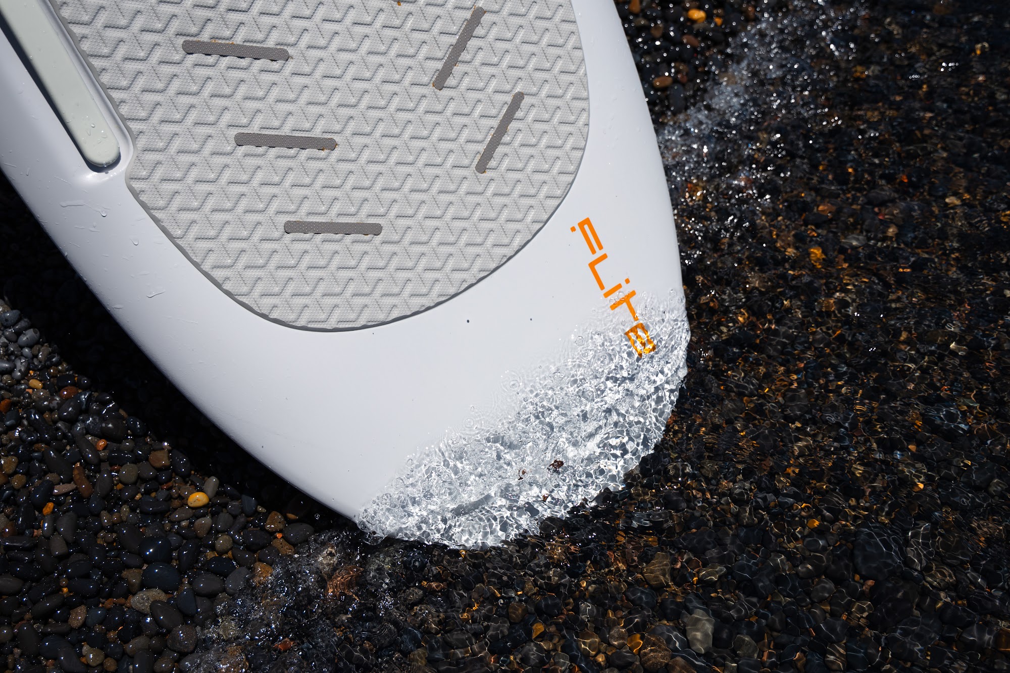 Two Fliteboard eFoils resting at the waterline on a pebble beach on Lake Tahoe's north shore, pines and blue sky behind