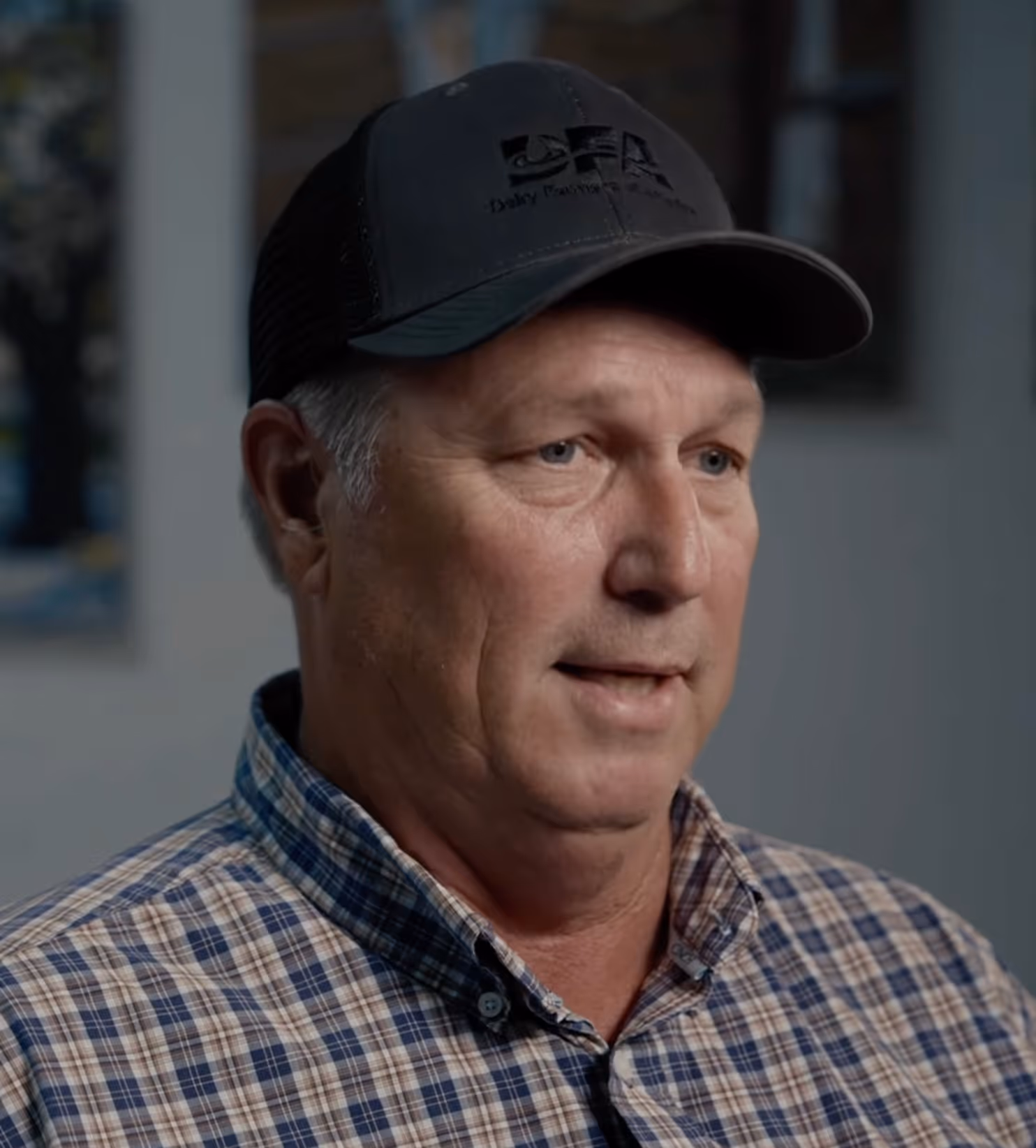 Middle-aged man wearing a black cap and a blue and beige plaid shirt, looking slightly to the right.