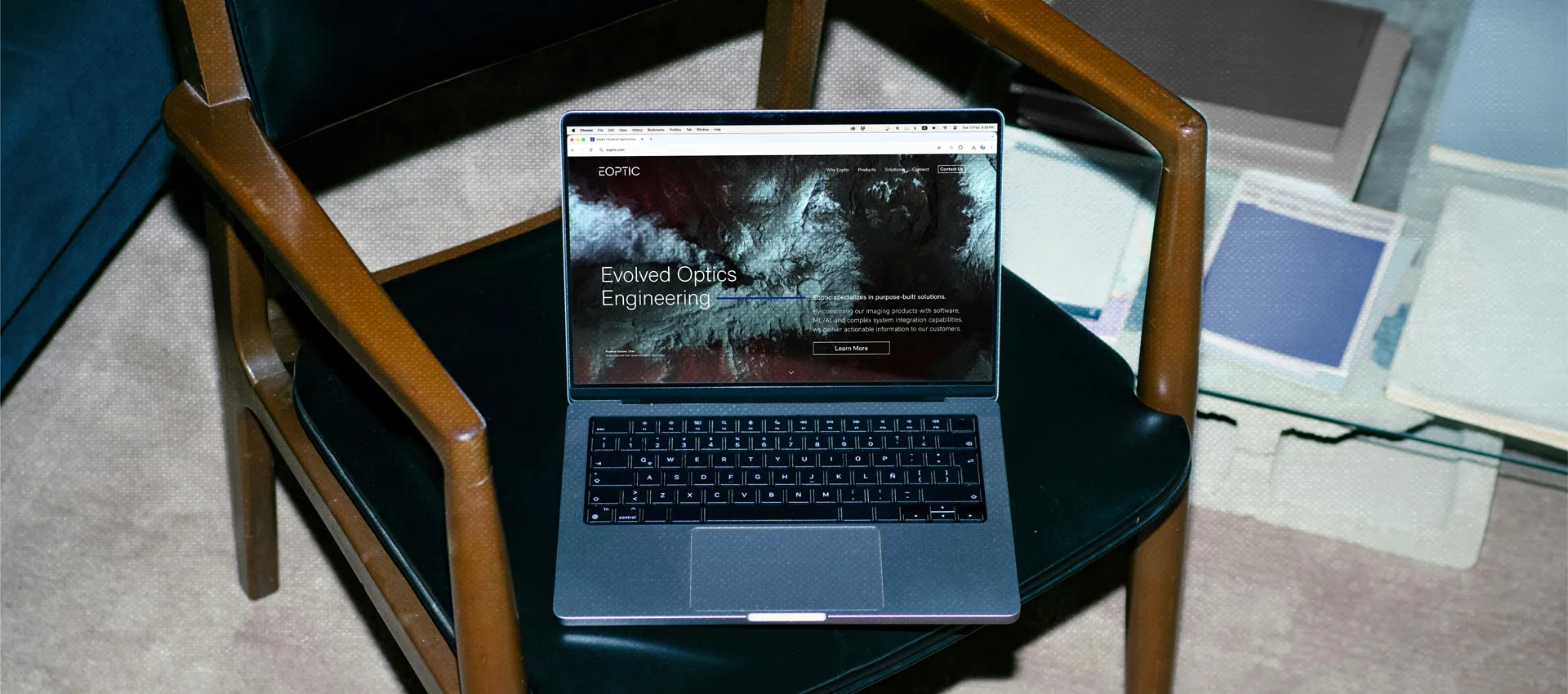 A Macbook laptop on an office chair showing the homepage of Eoptic's website