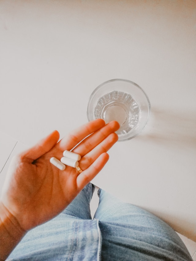 a person holding supplements in their hand next to a glass of water