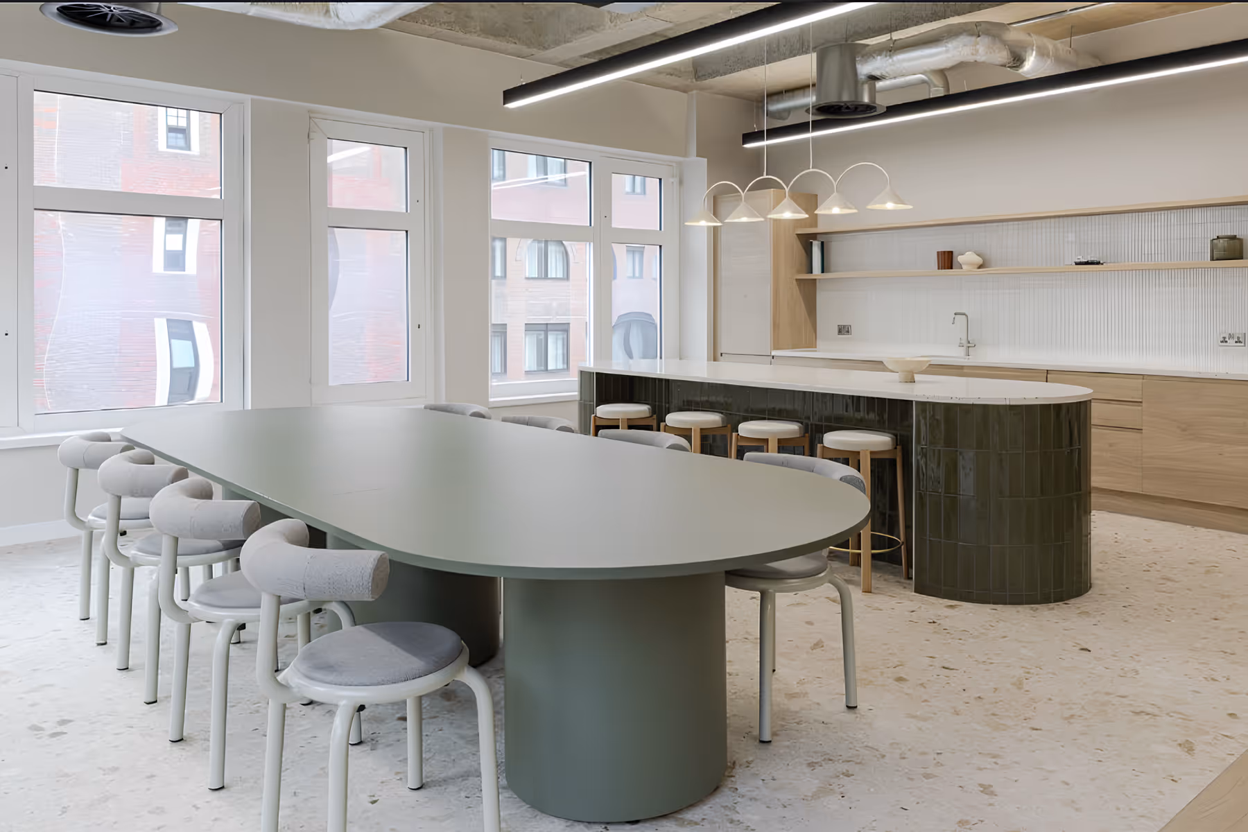 Modern office space with black mesh chairs around light wood desks, plants on desks, and partition curtains.