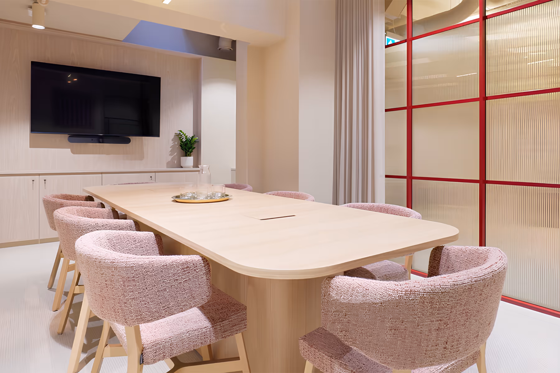 Modern office space with round white table and wooden chairs in foreground and long work tables with black mesh office chairs in background.