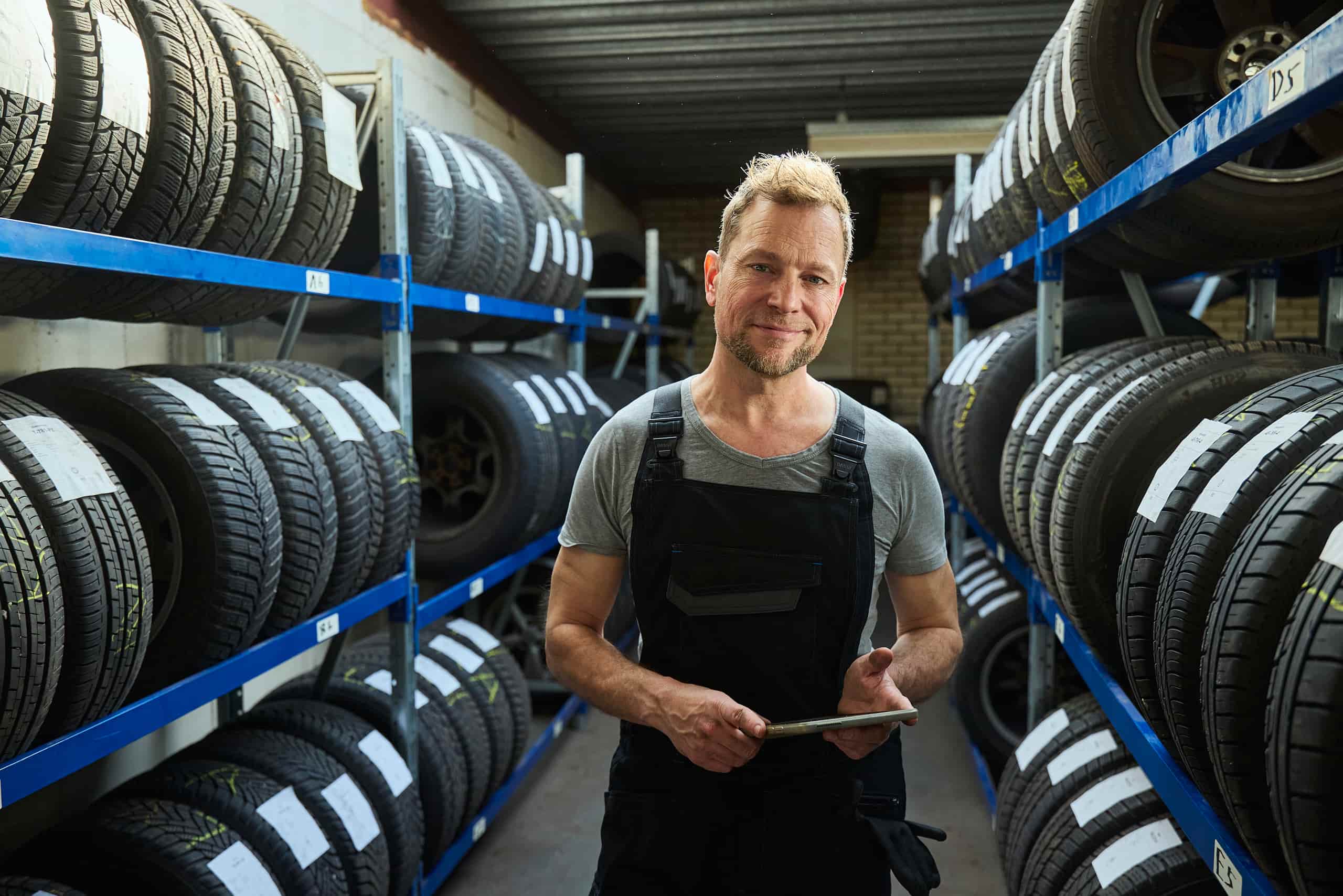 Garage ondernemer staat tussen autobanden voorraad
