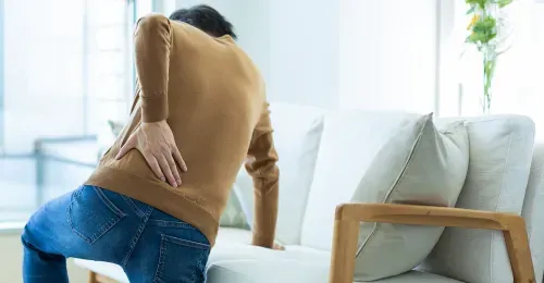 Mann erleidet Hexenschuss und stützt sich auf Sofa ab