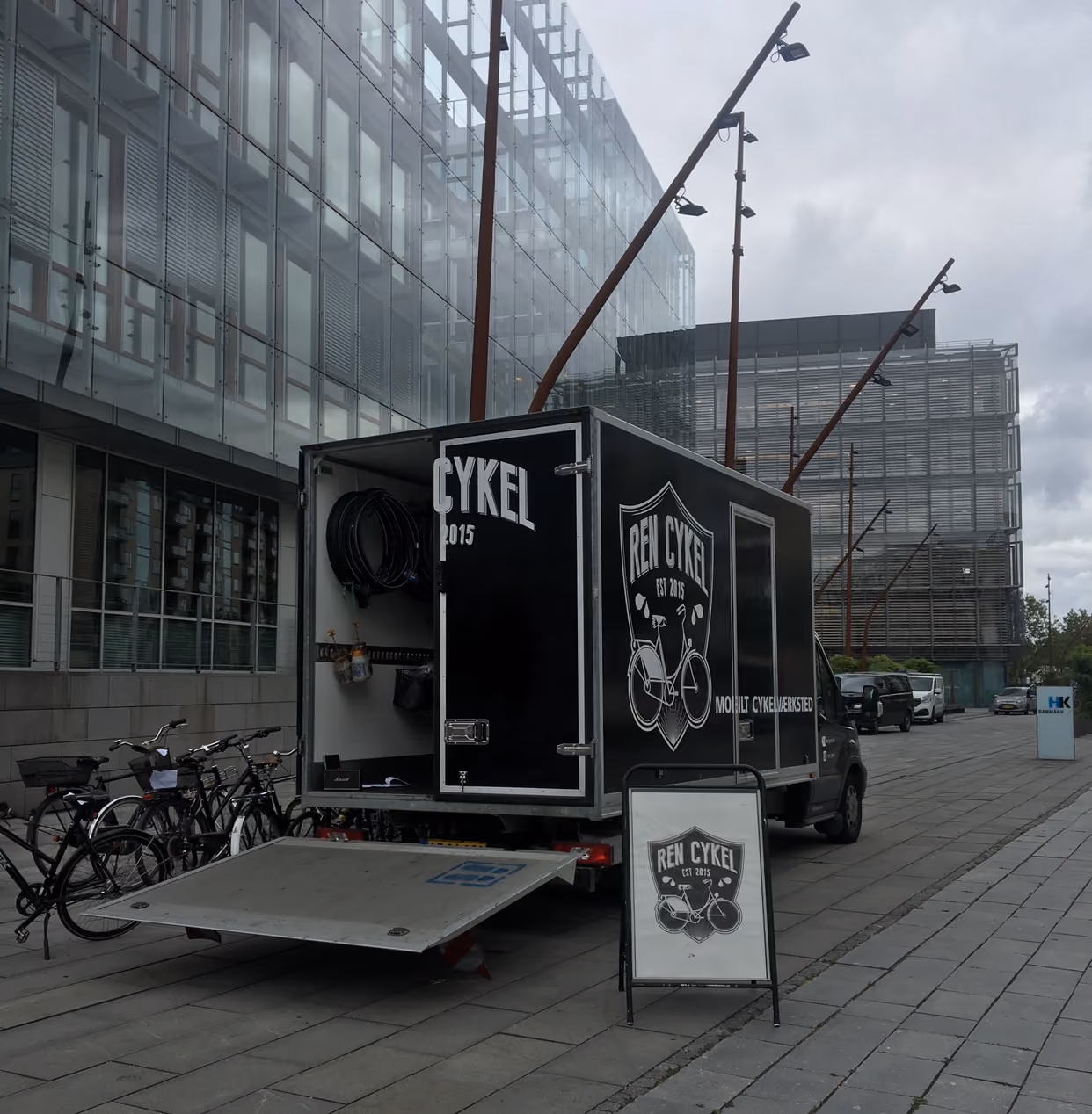 Mobilt cykelværksted fra Ren Cykel parkeret ved kontorbygning, klar til cykelservice og reparation.