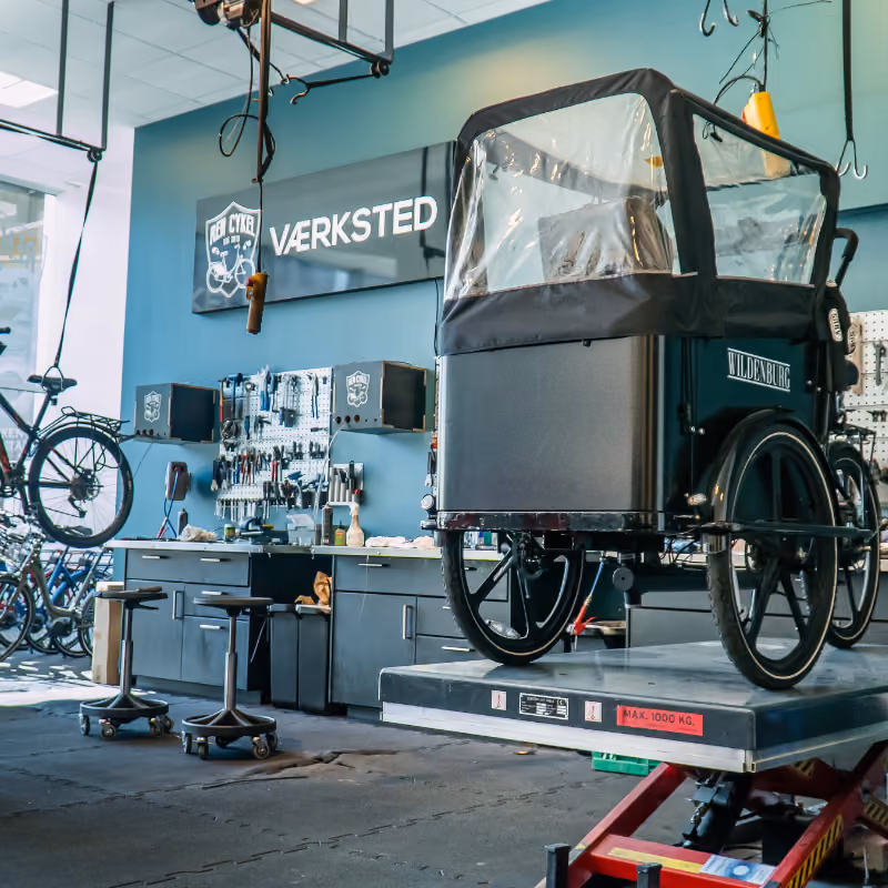 Wildenburg ladcykel på værkstedslift, omgivet af værktøj og reservedele til cykelservice og reparation.