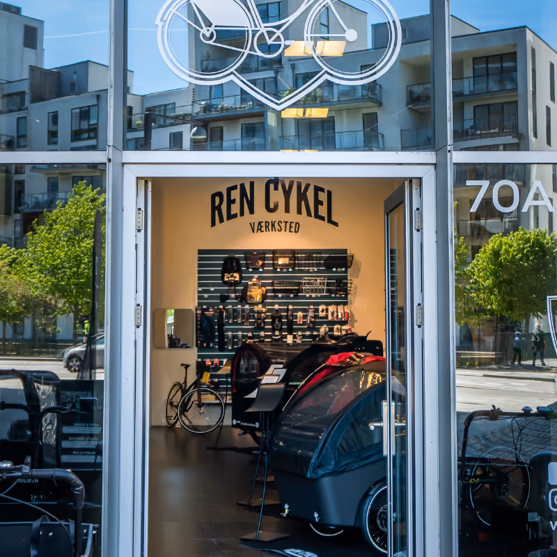 Indgang til Ren Cykel værksted med udstilling af ladcykler, reservedele og cykelreparationsudstyr.
