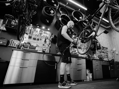 Cykelsmed laver cykelservice og lapning af cykel på travlt cykelværksted.