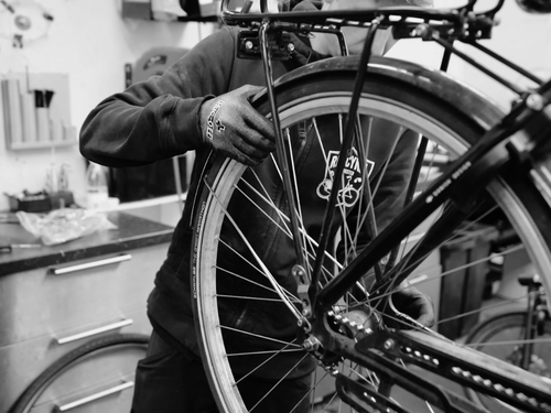 Cykelmekaniker laver cykelservice på baghjul med cykel skærm og bagagebærer på cykelværksted.