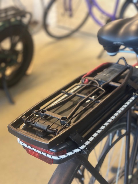 Nærbillede af en cykel bagagebærer monteret bag på en cykel. Bagagebæreren er udstyret med elastikker og spændebeslag, klar til fastgørelse af tasker eller andet bagage