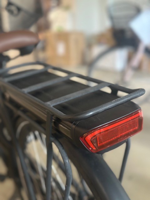 Robust cykel bagagebærer i sort metal, monteret bag på en cykel med integreret baglygte. Denne bagagebærer til cykel er ideel til daglig transport og kan nemt bære tasker, kurve eller barnesæder.