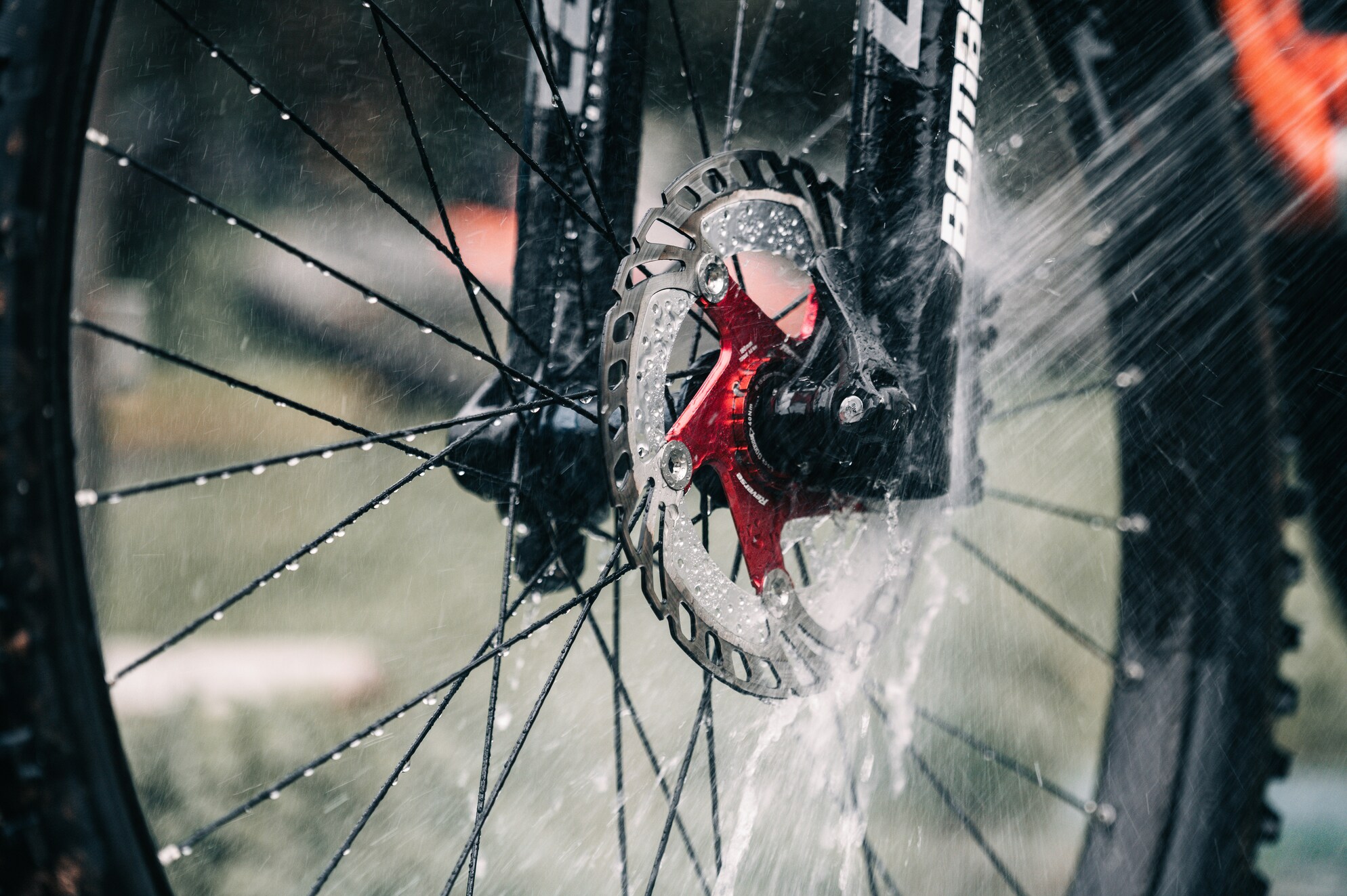 Detaljebillede af vask af cykel, hvor vand sprøjtes på cyklens skivebremser og hjul under grundig cykel rengøring. Dette er et eksempel på det man skal undgå at gøre