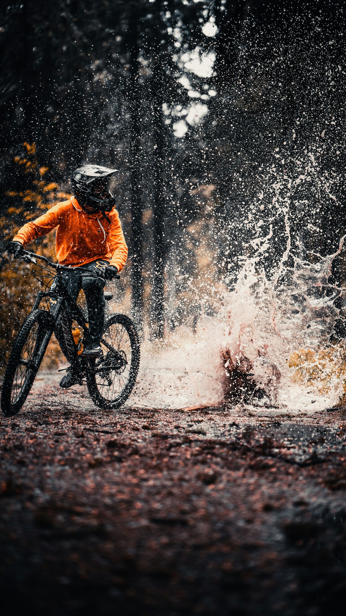 Mountainbiker kører gennem en stor mudderpyt i skoven med vand og snavs sprøjtende op omkring cyklen