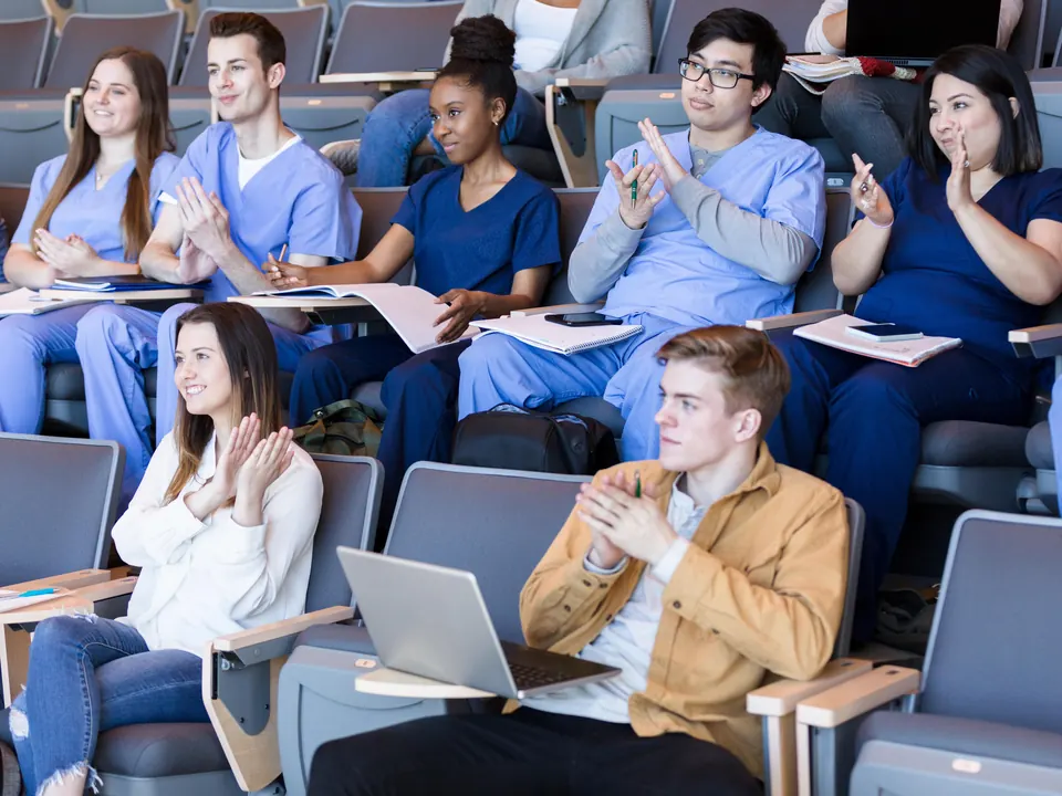 An audience in scrubs applauds in a lecture hall