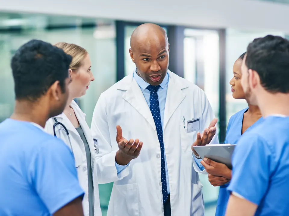 A clinician in a white coat talks with colleagues in scrubs
