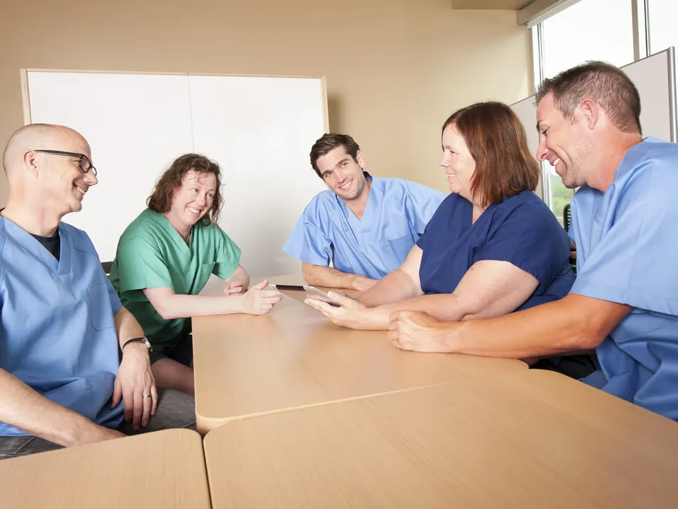Colleagues in scrubs talk around a meeting table