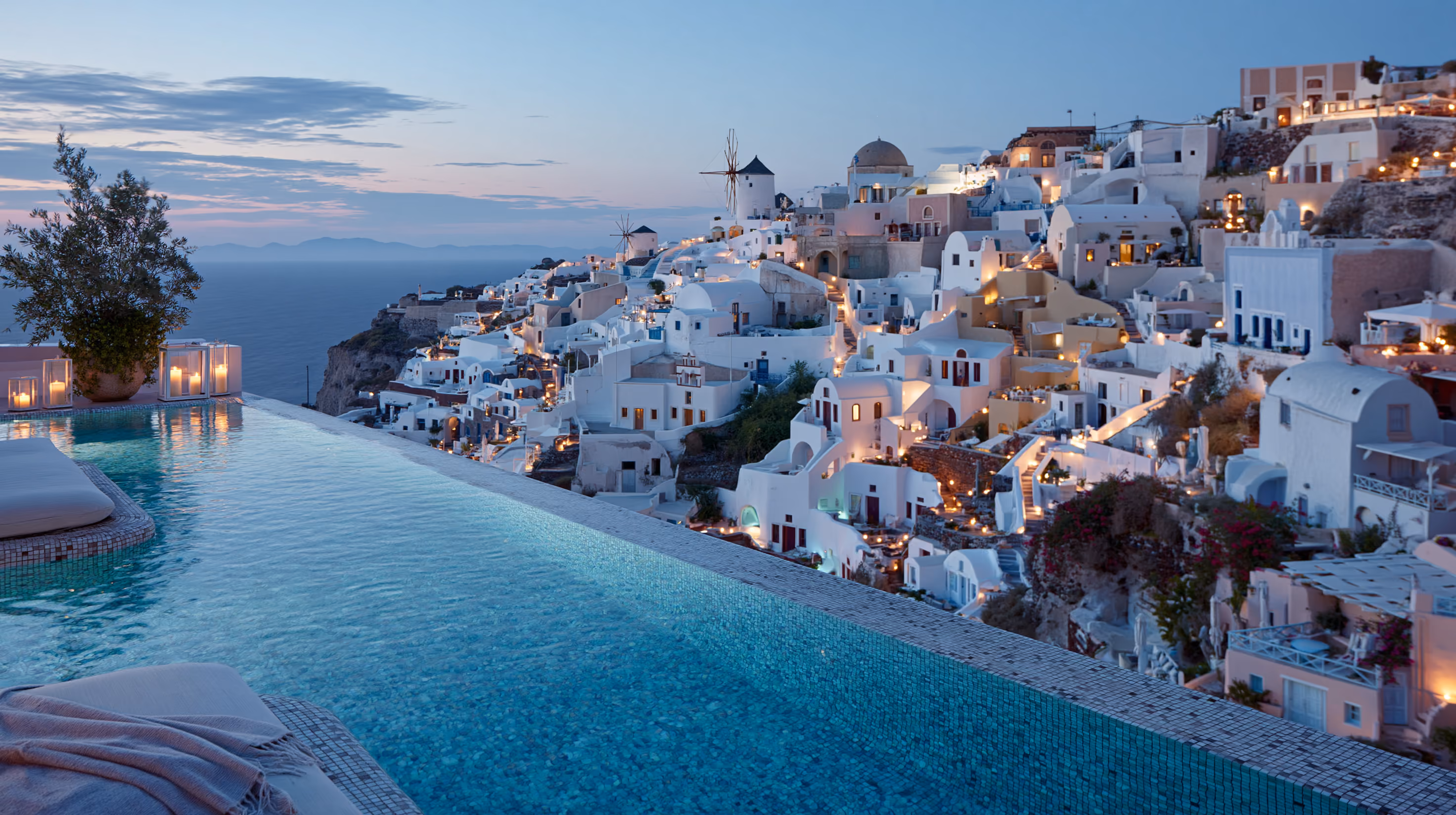 Infinity pool in Greece overlooking a whitewashed Cycladic village and windmills at dusk