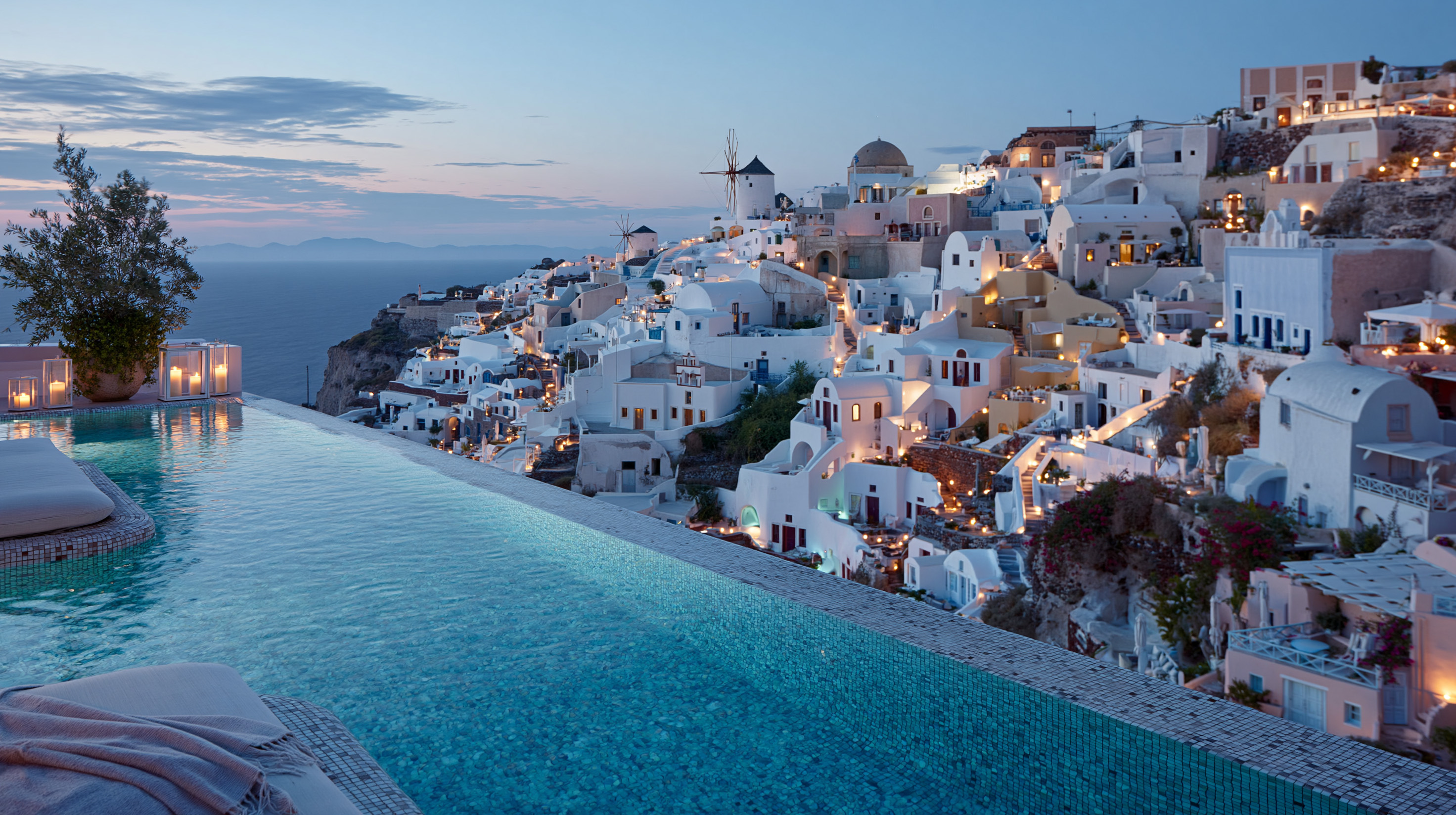 Infinity pool in Greece overlooking a whitewashed Cycladic village and windmills at dusk