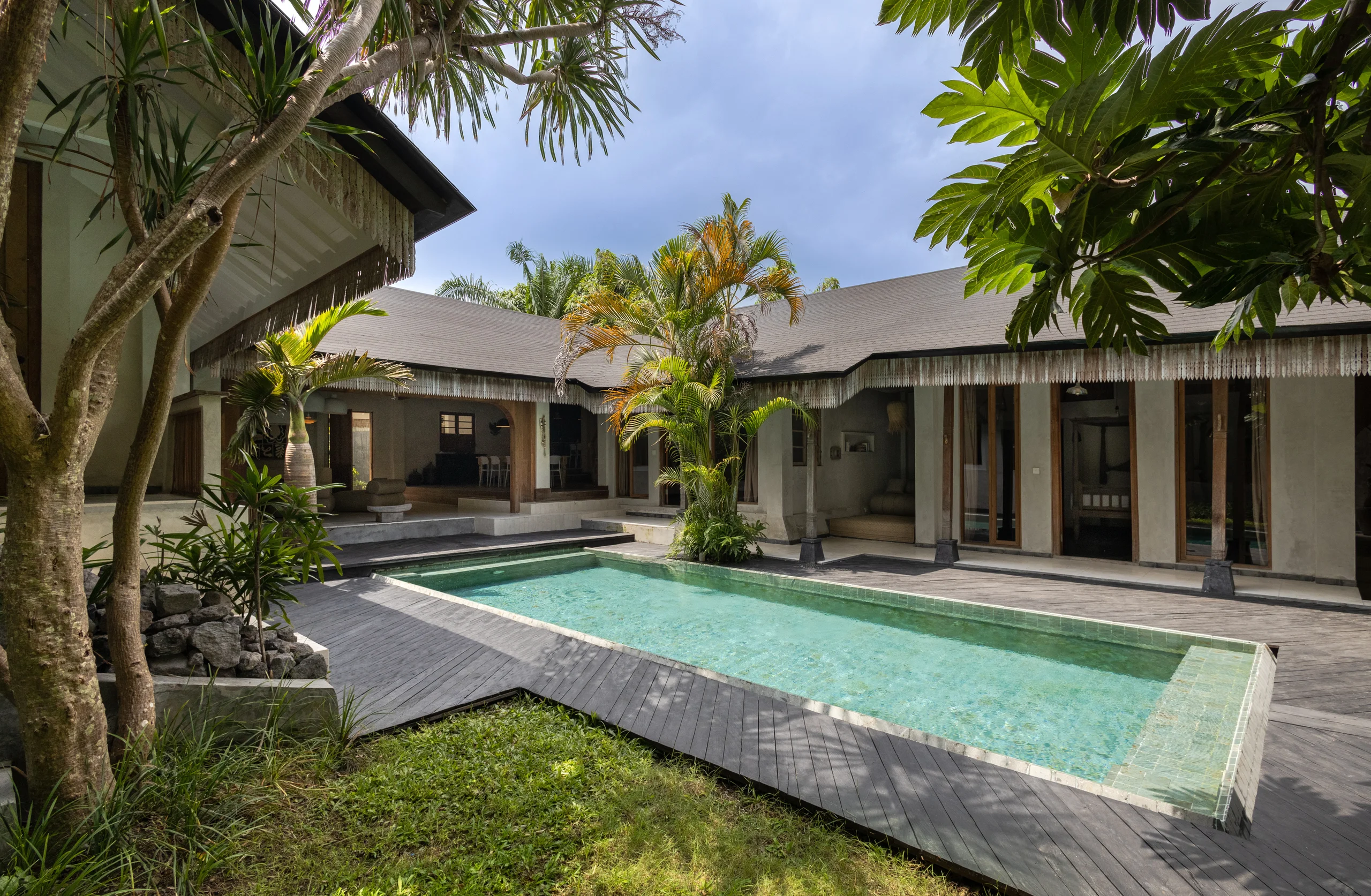 Single-story villa with a dark tiled hip roof and fringed eaves wrapped around an L-shaped pool and courtyard garden – Villa Santi, a 4-bedroom villa in Berawa, Bali
