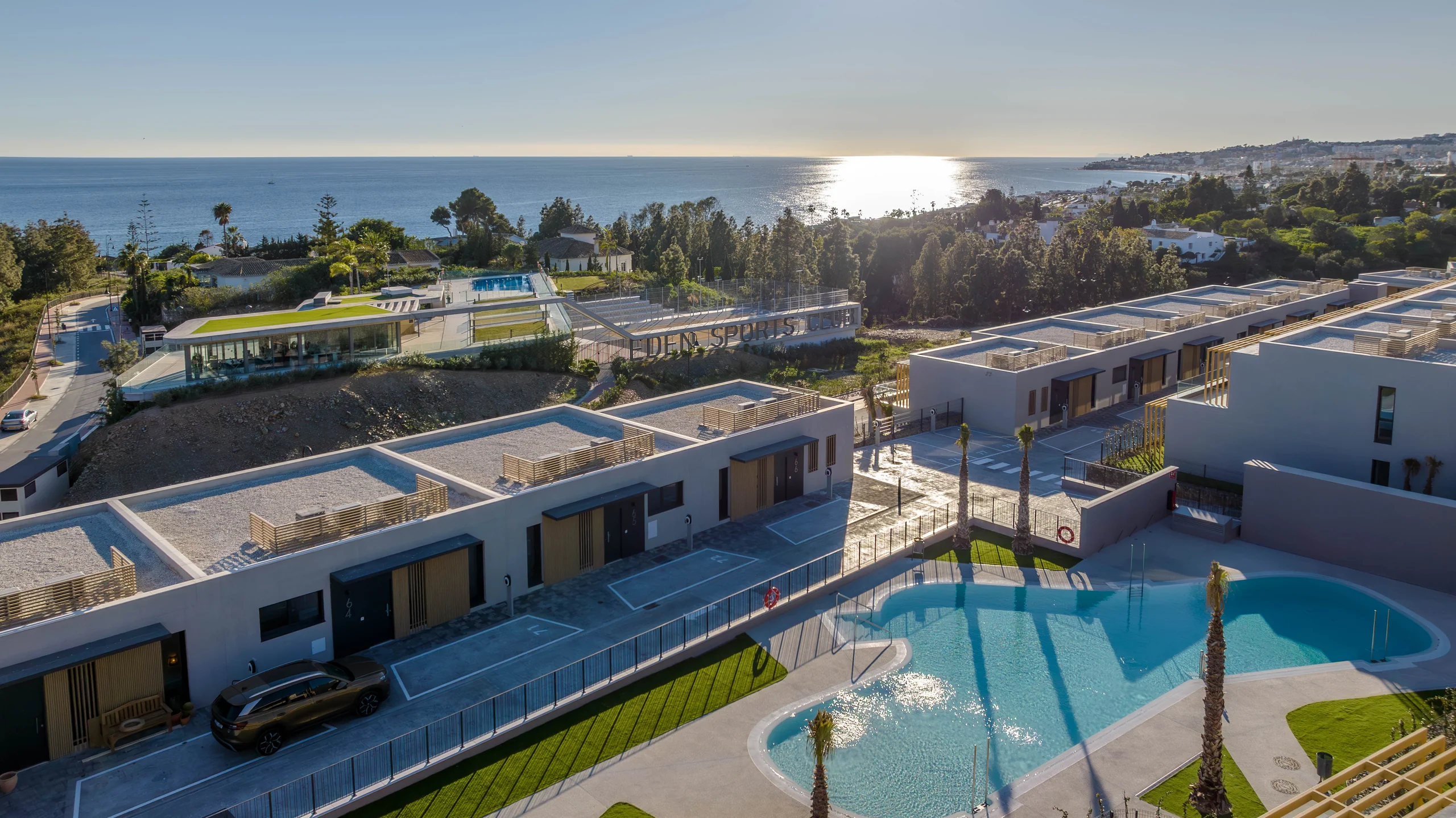 Aerial photo of a white townhouse development with a free-form swimming pool and the sea visible in the background – Evergreen Homes, a 3-bedroom apartment in El Chaparral, Mijas Costa, Málaga