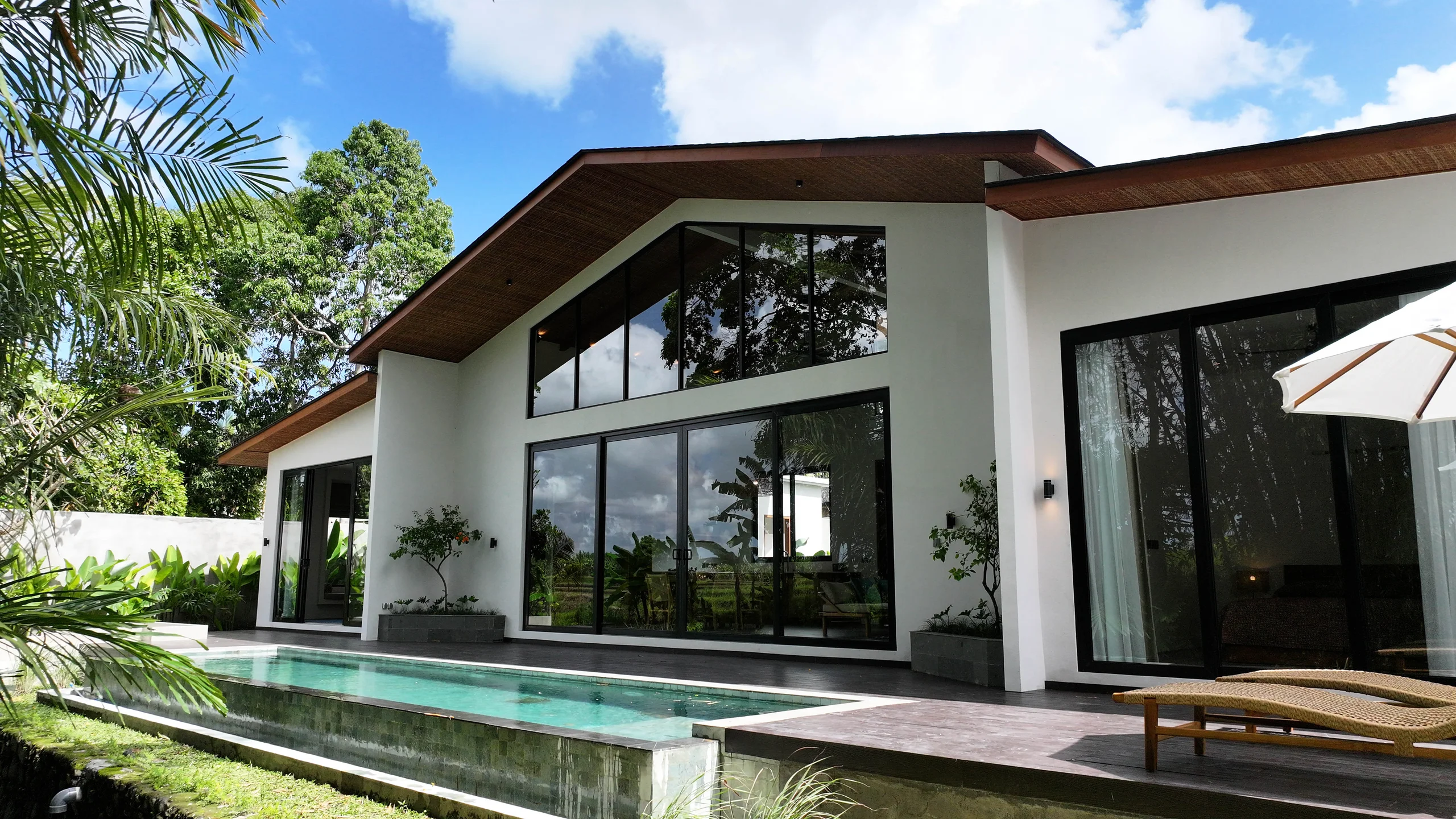 Double-height villa with a steep angled wood-lined roof overhang and glass walls beside a narrow lap pool and wood sundeck – Villa Arunia 1F, a 3-bedroom villa in Kaba Kaba, Bali