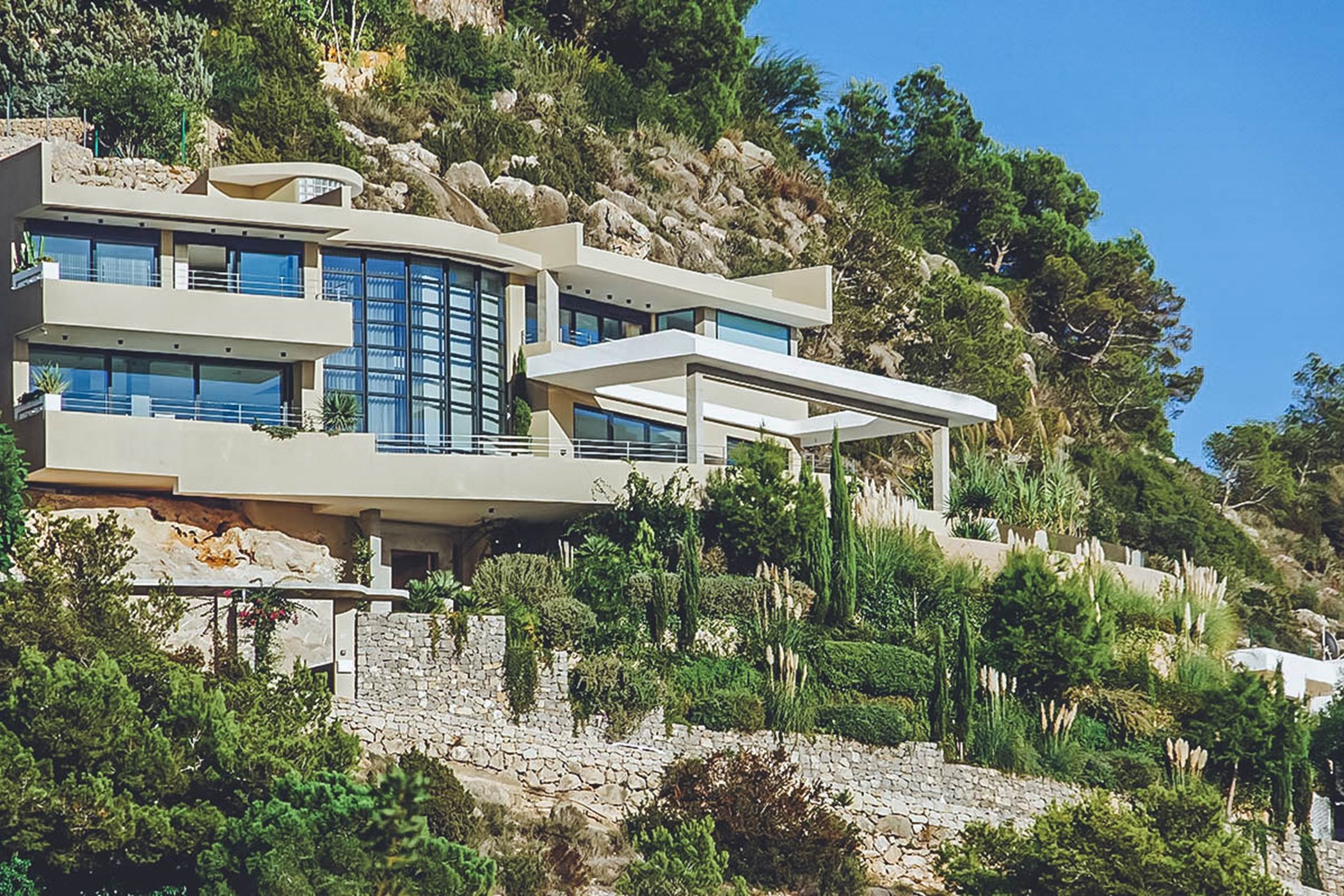 Contemporary cliffside villa with cantilevered balconies and floor-to-ceiling glass, set into a pine-covered rocky hillside – Villa Abigail, a 4-bedroom villa