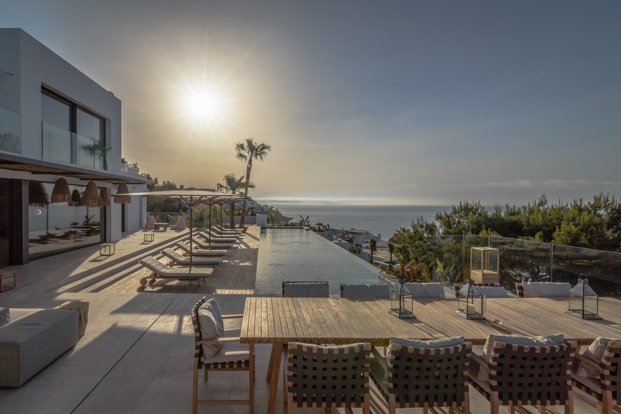 Terrace dining table and row of sunloungers beside an infinity pool at sunrise with the sea and coastline visible beyond – Can Olivera, a 5-bedroom villa