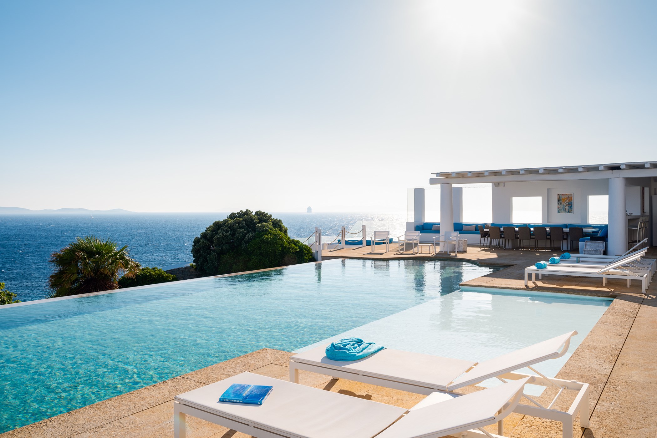 Clifftop infinity pool overlooking the open sea with distant islands, white sun loungers in the foreground and a pergola-covered terrace with dining and lounge seating – Villa Sea-Front, a 7-bedroom villa
