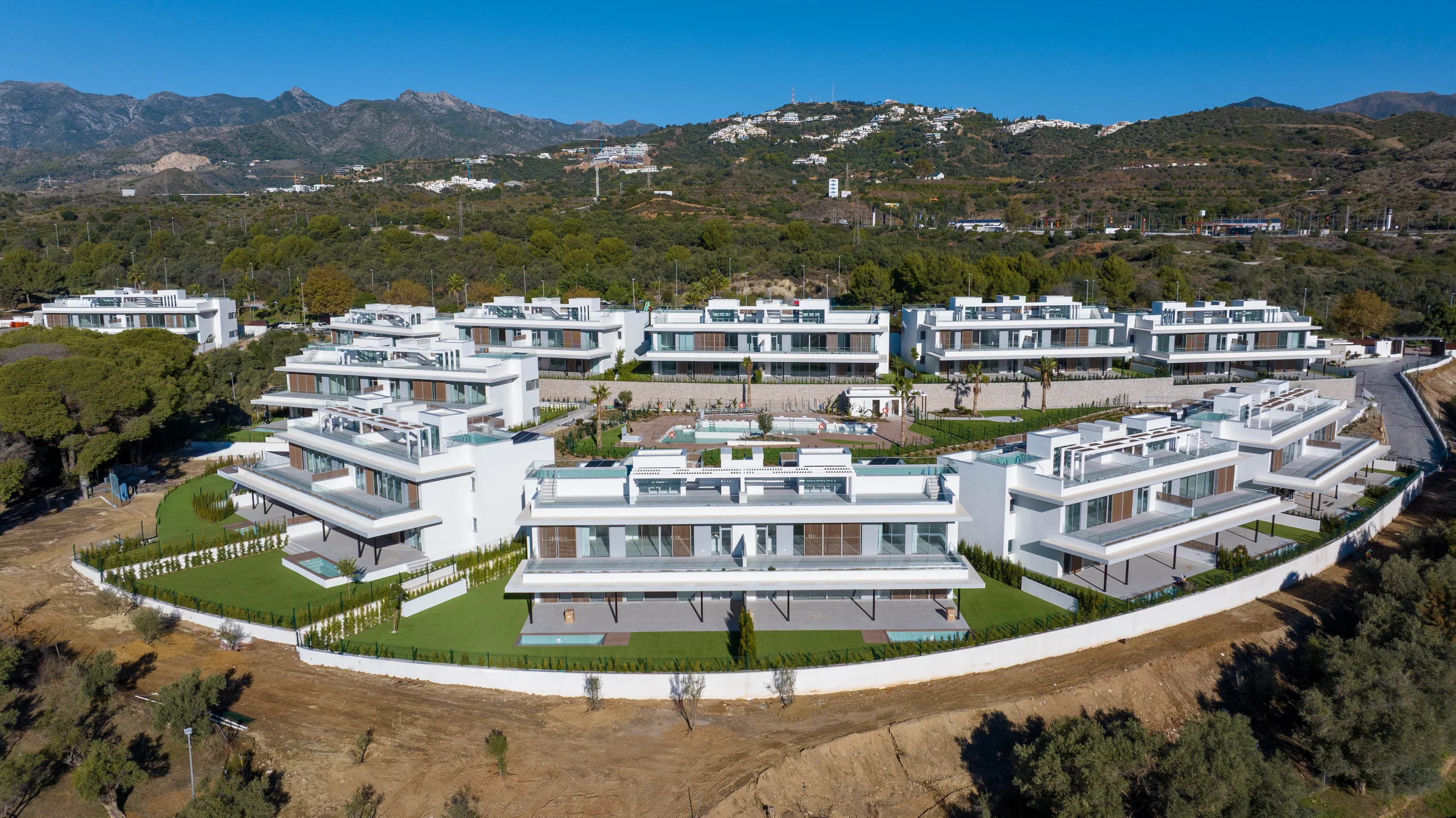 Aerial view of stepped white low-rise apartment blocks with private plunge pools on a hillside below distant mountains – Santa Clara Homes, a 3-bedroom apartment in Santa Clara Golf, Marbella, Málaga
