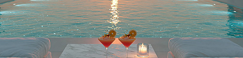 Two cocktails and a candle on a poolside table with the sunset reflecting on the water – Georgia