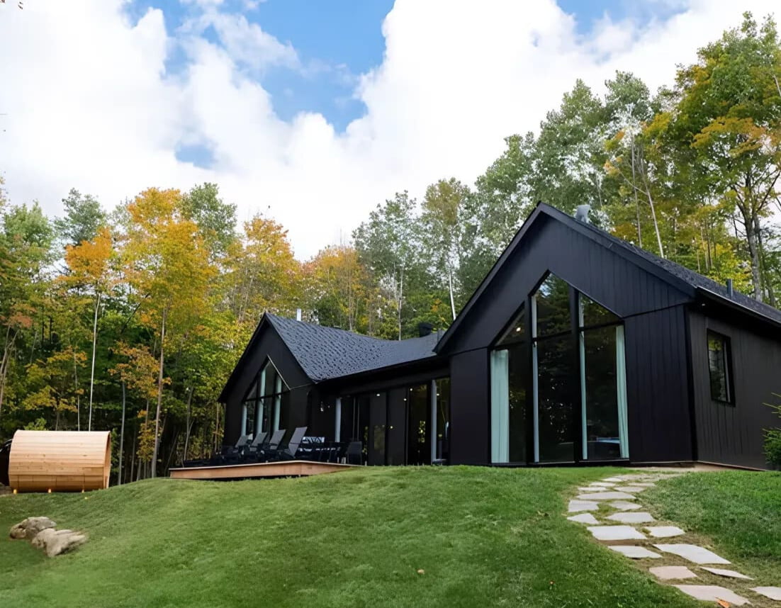 HM Vacation rentals: Black Diamond Kanata Tremblant: A modern black cabin with a hot tub and sauna, set against an autumn forest.