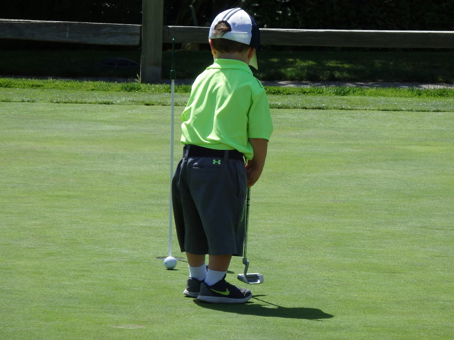 Un jeune garçon se tient sur un green de golf avec un putter et une balle.